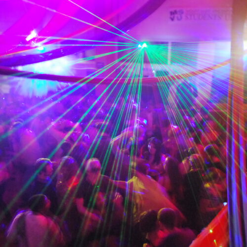 School events DJ hire - College dancefloor with laser lights, DJ booth, and energetic students dancing, capturing the excitement of a campus party.