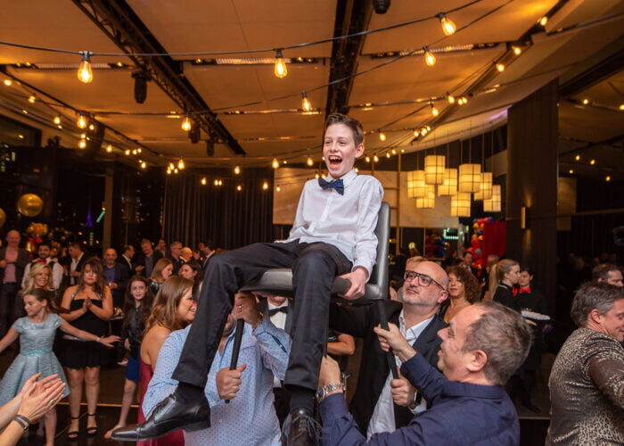 A boy being joyfully lifted on a chair during his Bar Mitzvah celebration. DJ Events and Parties.